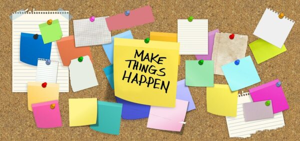 Bulletin Board with multicolored post-its pinned to it including a yellow one that reads, "Make Things Happen."